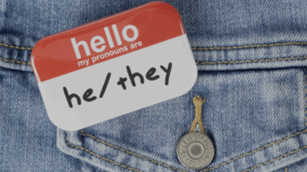 A name tag on a denim jacket that reads, "Hello, my pronouns are he/they."