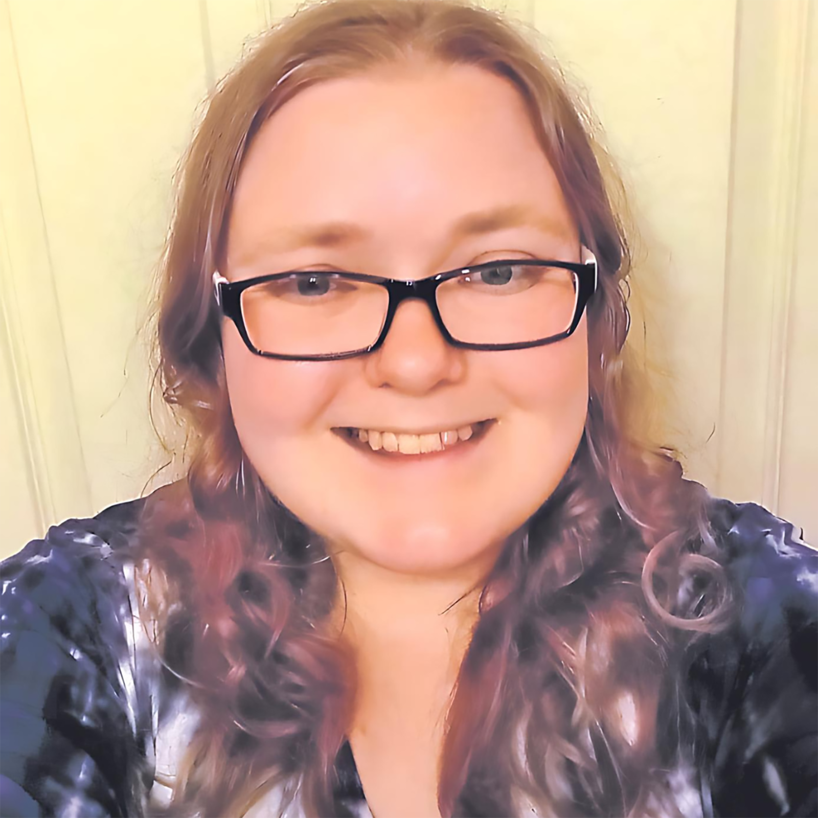 Nonbinary Arkansan with blonde hair and black glasses smiling in front of a white door.