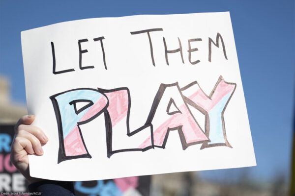 Sign reading Let Them Play in pink, blue and white colors.