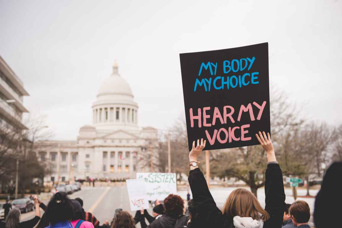 Woman holds a rally sign reading "My body my choice hear my voice" in front of the Arkansas capitol building