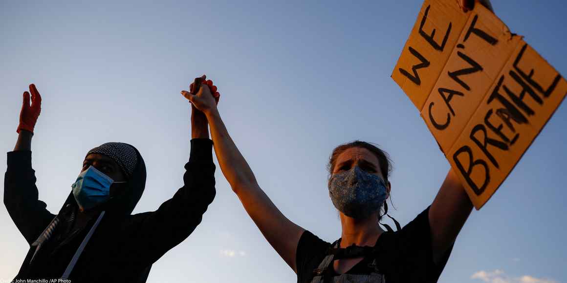 A man and a woman holding a sign reading "We can't Breathe"