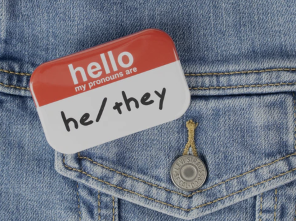A name tag on a denim jacket that reads, "Hello, my pronouns are he/they."